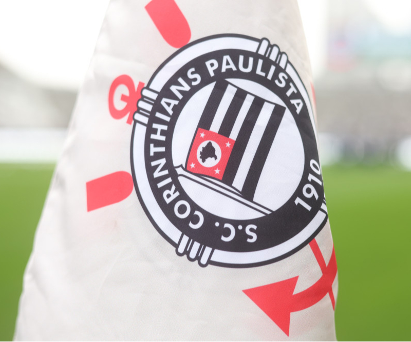 Fachada da sede do Corinthians com bandeiras do clube ao fundo.